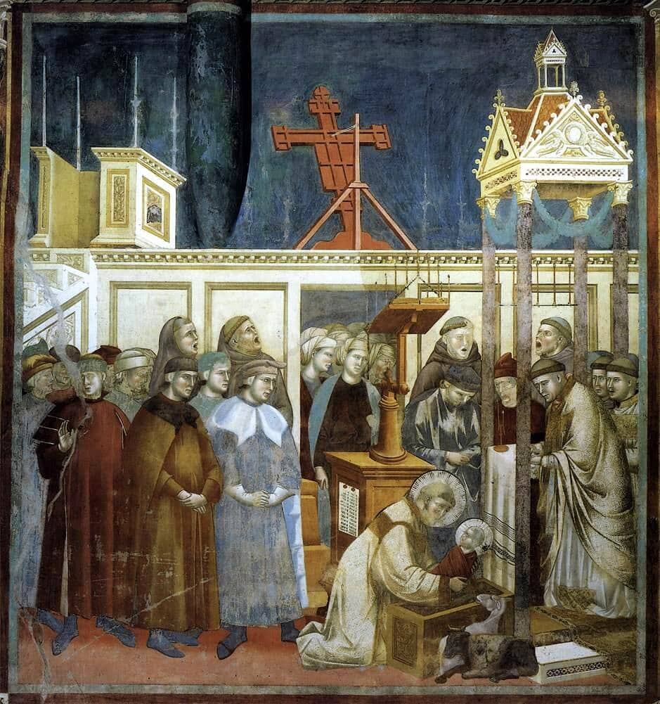 A fresco of Saint Francis at Greccio: inside a church, Francis kneels at a manger holding the baby Jesus, beside a small ox and donkey, while friars sing and townspeople watch.